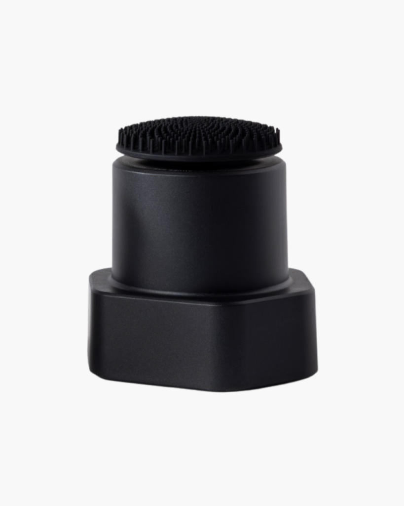 Brosse nettoyante visage en silicone noir avec socle hexagonal, photographiée seule sur fond blanc, vue de trois quarts.