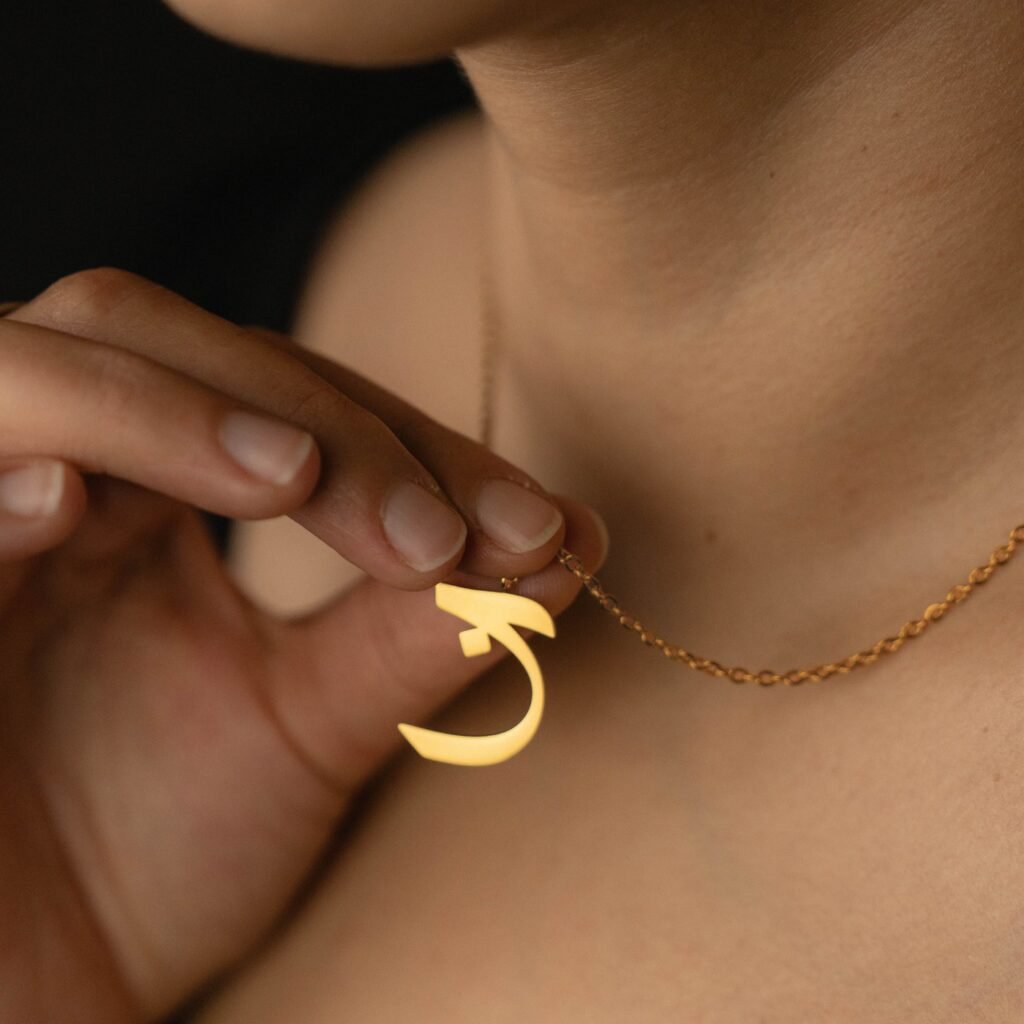 Pendentif doré en forme de lettre arabe porté sur une chaîne