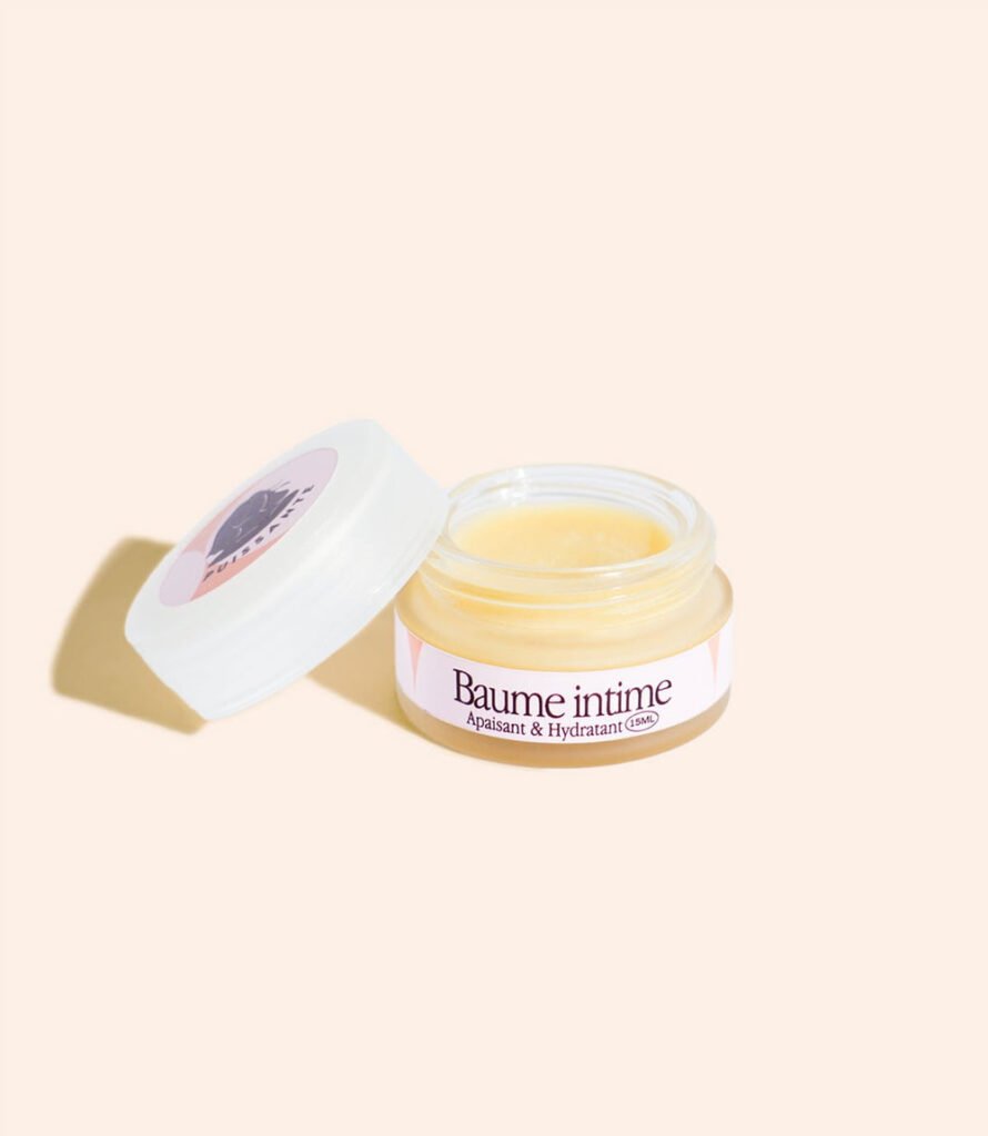 Pot de baume intime Puissante ouvert, couvercle posé à côté, révélant le baume jaune à l'intérieur, sur fond beige.