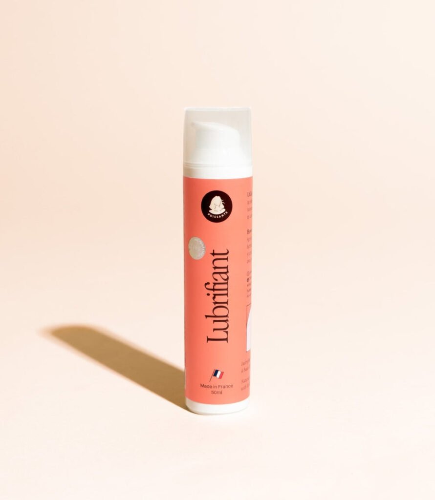 Flacon de lubrifiant intime Puissante debout sur fond beige, étiquette corail visible avec le nom du produit, le logo de la marque et l'indication Made in France 50ml.