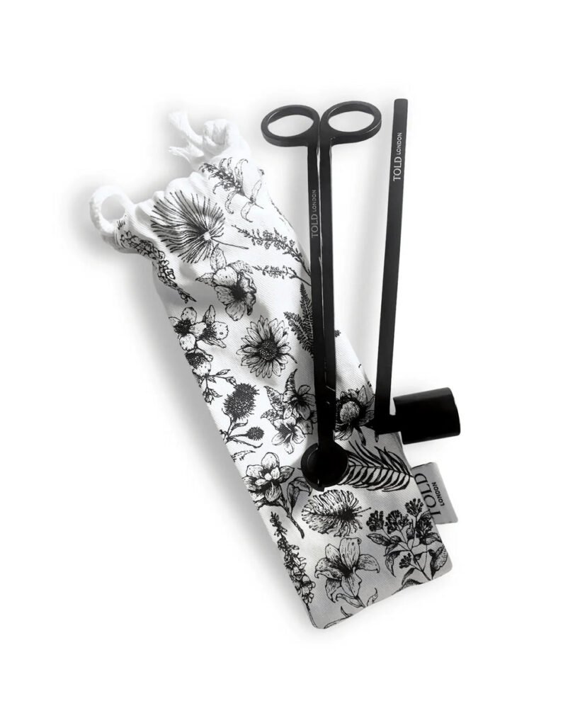 Coupe-mèche, éteignoir noir et pochette en tissu à motifs floraux estampillée Told London, sur fond blanc.